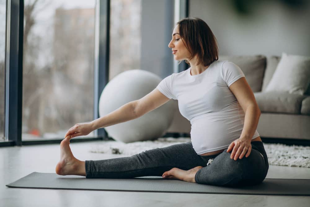 Pregnant woman stretching on yoga mat in bright living room