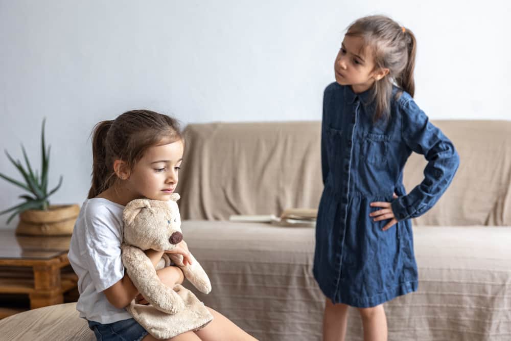 Two young siblings sitting together while parent comforts them