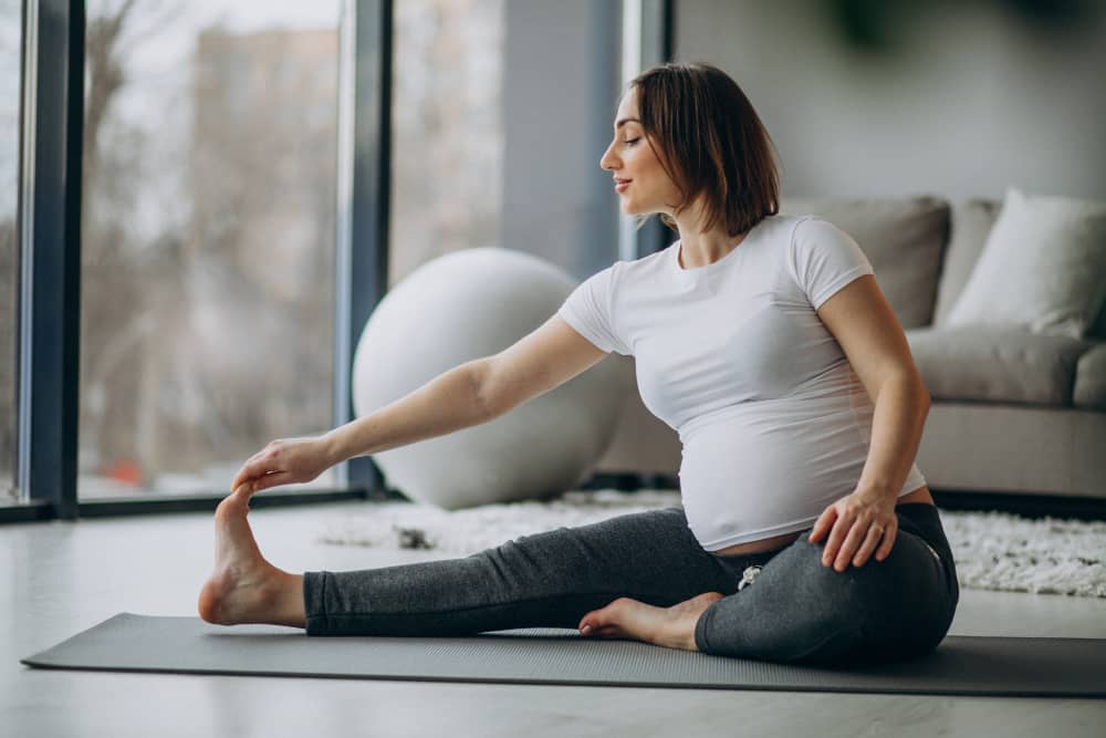 Pregnant woman stretching on yoga mat in bright living room