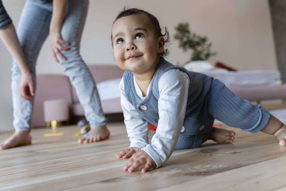 Smiling baby crawling on a soft mat reaching toward a toy